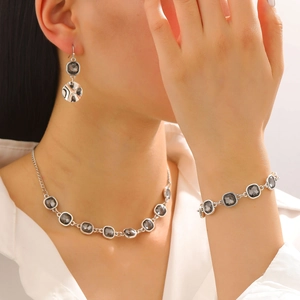 Detail of silver-tone necklace set featuring faceted square grey crystals on a model