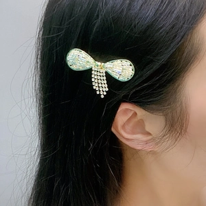 Detail of a light green bow hair clip with sparkling rhinestones and long tassel fringe
