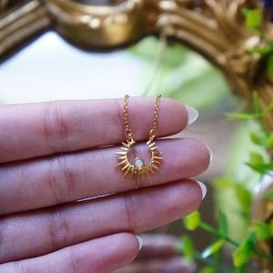 Exquisite gold sun necklace with white opal stone held by hand, vintage aesthetic