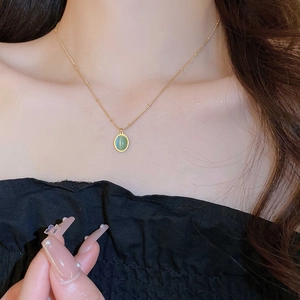 Detail showing an elegant gold chain necklace with an oval green opal pendant on a model