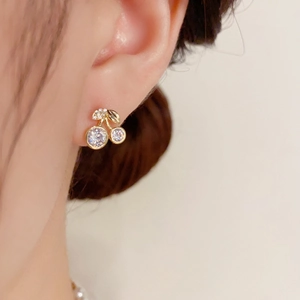 Macro view of gold cherry stud earrings with sparkling white zircons on a model