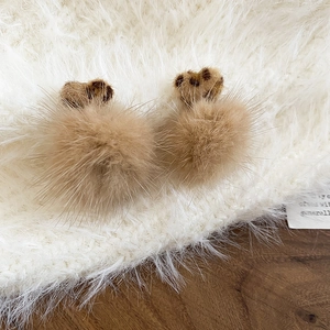 Close-up of brown plush bear-shaped pompom earrings on soft faux fur surface