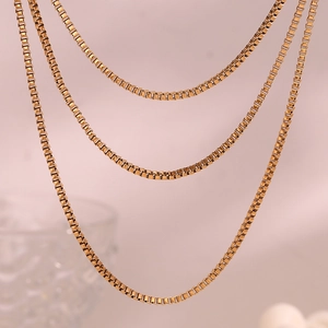 Macro view of tiered 18K gold plated stainless steel box chains on soft pink background