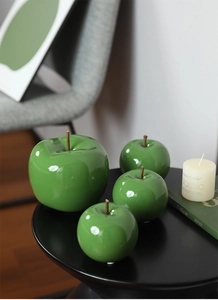 Détail de quatre pommes en céramique verte brillante sur une petite table noire déco