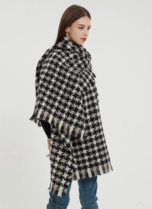 Detail of a thick oversized houndstooth shawl with fringe tassel edges in black and beige