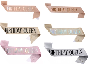 Multiple colors of Birthday Queen glitter sashes featuring elegant sequins and gold safety pins