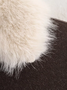 Macro shot of faux fur pom-pom on cream white woolen coat with sharp texture details