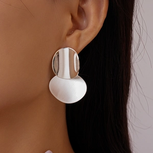 Close-up of geometric oval silver drop earrings featuring brushed and polished metal textures