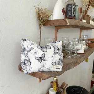 Detailed close-up of white lace butterfly cosmetic bag on a wooden shelf in home setting