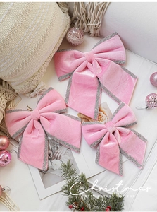 Three pink velvet Christmas bows with silver glitter edges on a beige knit pillow
