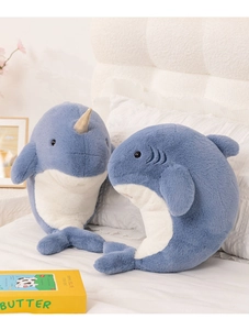 Close-up of soft blue narwhal and shark plush toys on a bed with cozy home decor