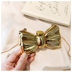 Detail showing high-gloss gold metallic bow-shaped evening clutch with delicate chain strap