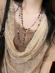 Detail of layered beaded necklace with silver flower charms on a beige lace garment