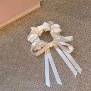 Détail d'un chouchou en satin blanc avec un long ruban sur tissu en lin texturé