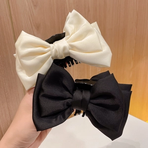 Detail of cream and black satin bow hair claws with elegant silk texture and glossy finish