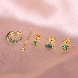 Detail of S925 sterling silver gold earrings set with emerald green stones on pink silk