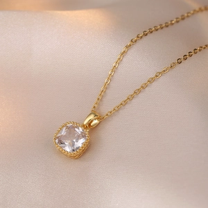Détail d'un pendentif en zircon carré sur une chaîne dorée posée sur de la soie champagne