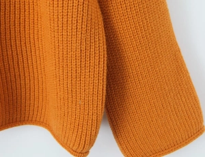 Détail du pull en maille orange montrant la texture côtelée sur l'ourlet et les poignets