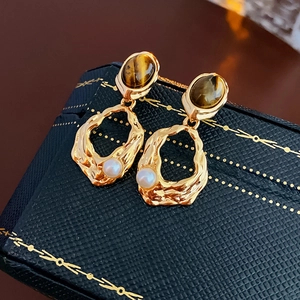 Macro detail of gold-plated tiger eye earrings with pleated metal and white pearl