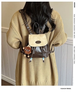 Mini backpack in coffee and beige leather worn by a model against a wooden wall