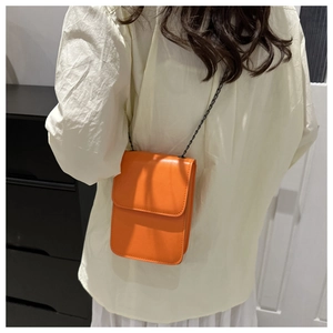 Side view of a model wearing a small orange crossbody chain bag with leather texture
