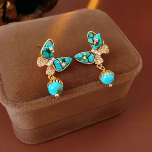 Boucles d'oreilles papillon dorées avec turquoise et perles sur velours luxe