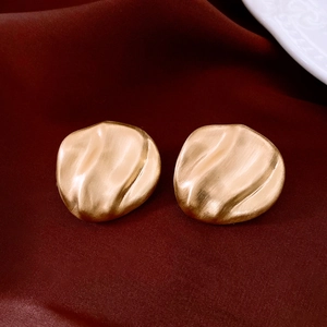 Detail of gold brushed metal oval earrings with wavy texture on red velvet background