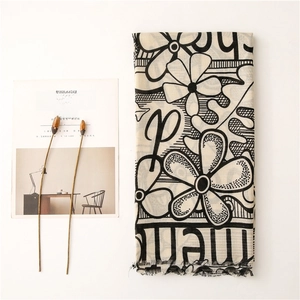 Detailed flat lay of a floral print cotton scarf with fringe edges and stylized letters
