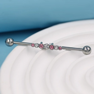Gros plan d'un piercing industriel avec cristaux roses et clairs sur un support blanc
