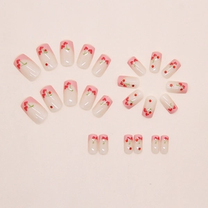 Detail of pink French press-on nails with cherry and heart designs on a beige background