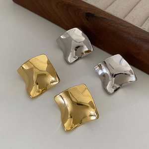 Irregular wave geometric stud earrings in gold and silver finish on white surface