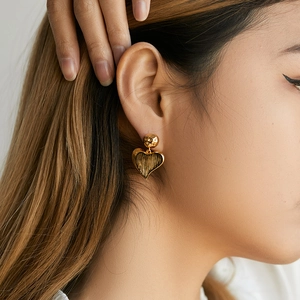 Close-up of golden heart earrings with textured vintage finish on female model