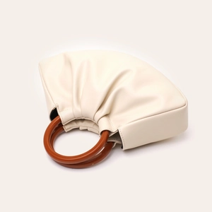 Detail of a beige pleated cloud bag with elegant round brown wooden handles and PU leather