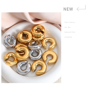 Detailed view of polished gold and silver C-shaped ear cuffs on a ceramic tray
