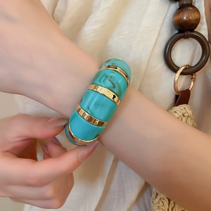 Detail of blue acrylic marbled bangle with gold-tone accents on a model wrist