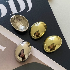 Macro shot of minimalist metallic oval stud earrings in glossy gold and silver finishes