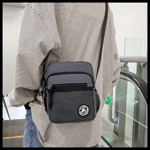 Detail of dark grey crossbody square bag featuring mesh pocket and branded logo patch