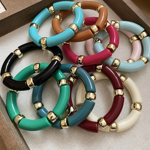 Detailed view of colorful acrylic tube bead bracelets with golden spacers on linen