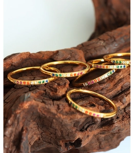 Macro shot of six gold rings with colorful gemstones on a textured wood surface