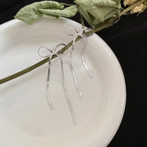 Dettaglio di orecchini a fiocco argento con lunghe nappe su un piatto di ceramica
