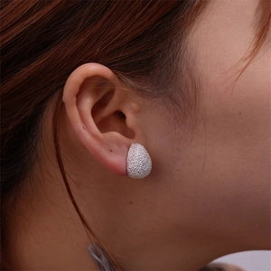Macro shot of silver teardrop stud earrings with textured matte finish on model