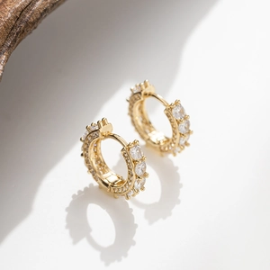 Detail of gold hoop earrings with pavé zircons and secure clasp on a natural wood block