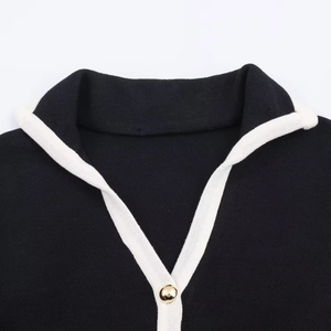 Detailansicht der schwarzen Strickjacke mit weißem Rand und goldenem Metallknopf-Akzent