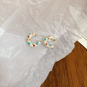 Detail of C-shaped white enamel earrings with colorful dots and golden metallic edges