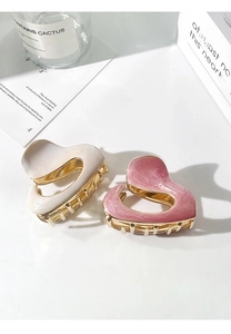 Detail of cream and pink enamel shark hair clips with golden metal teeth on a white surface