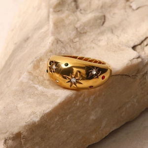 Detailed shot of a wide gold ring with star engravings and colorful zircons on a rock