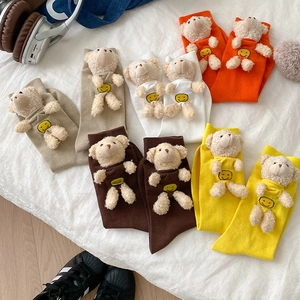Cute knitted socks with 3D teddy bear dolls in various colors on white bedding