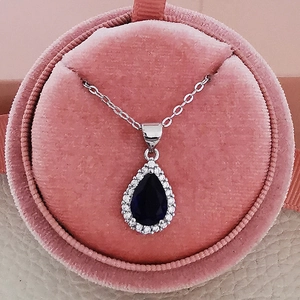 Close-up of a pear-shaped blue zircon necklace in a pink velvet jewelry box