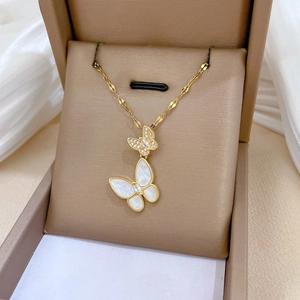 Macro detail of gold necklace featuring zircon-encrusted and mother-of-pearl butterfly pendants