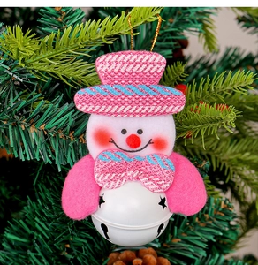 Pink fabric snowman ornament with star-cutout metal bell hanging on a green pine branch